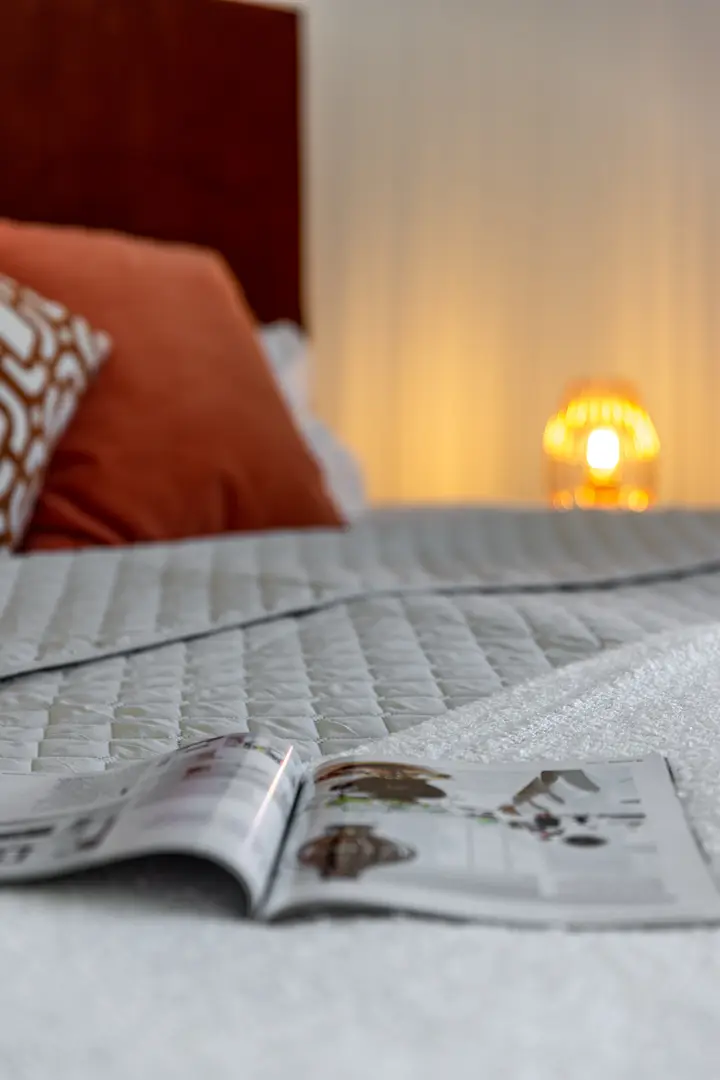Bett mit Tagesdecke und Zeitschrift im warmen Licht