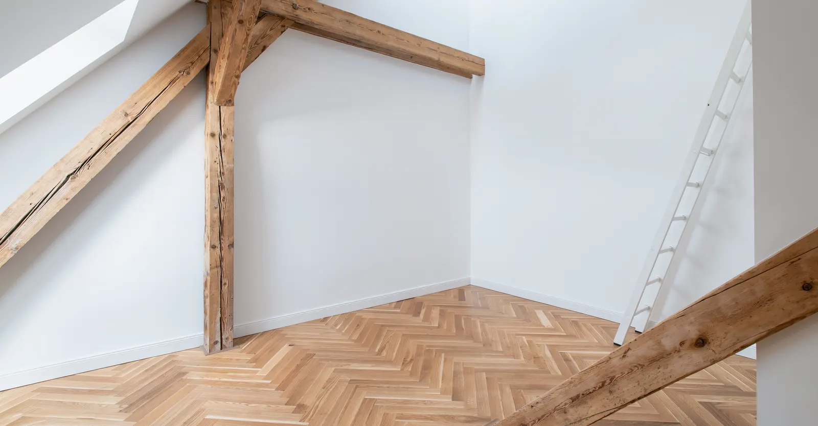 Leeres Dachgeschoss mit Holzbalken und Fischgrätparkett vor dem Home Staging