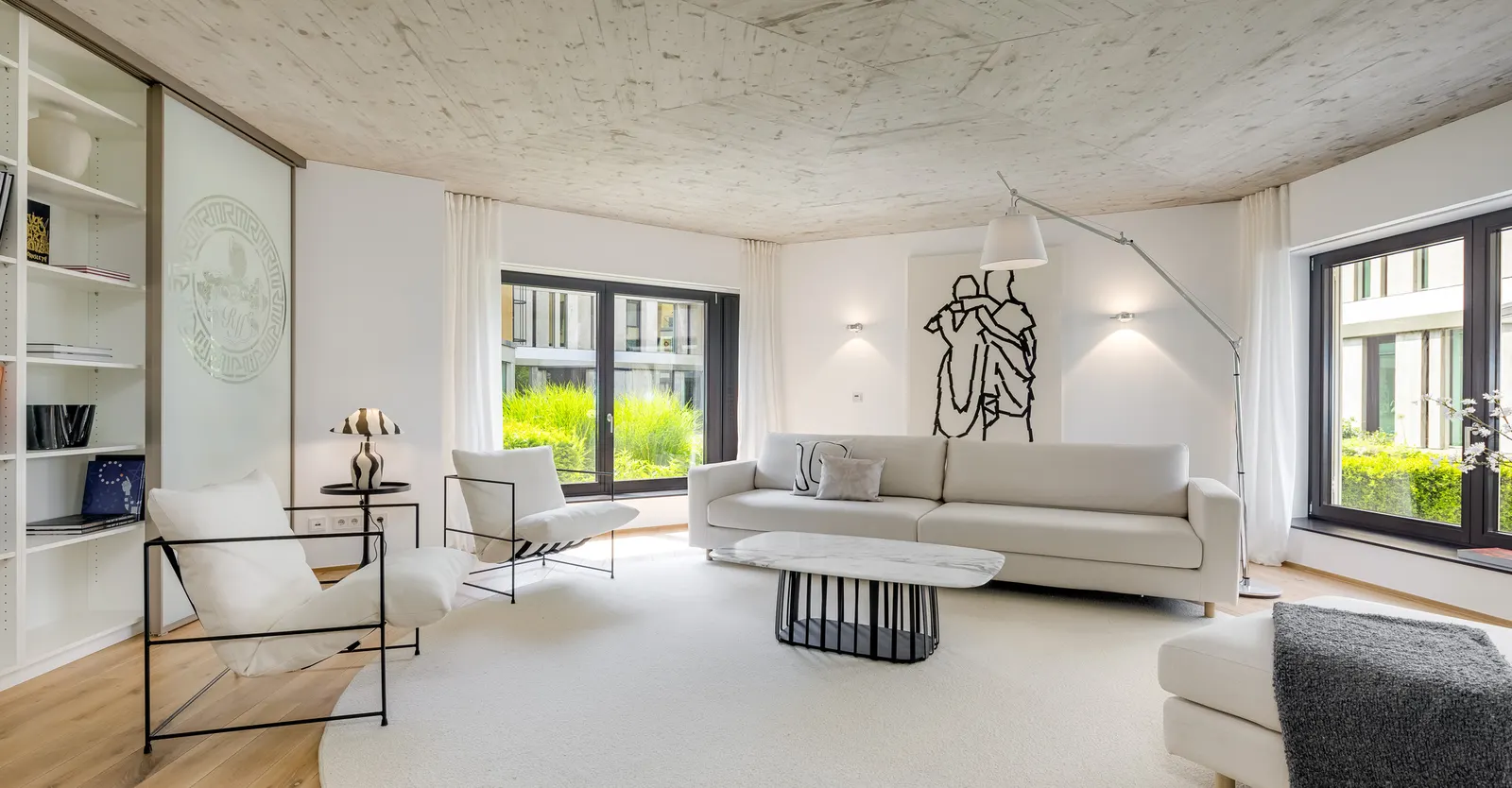 Wohnzimmer mit Sofa, Sesseln und Bogenleuchte unter einer Sichtbetondecke