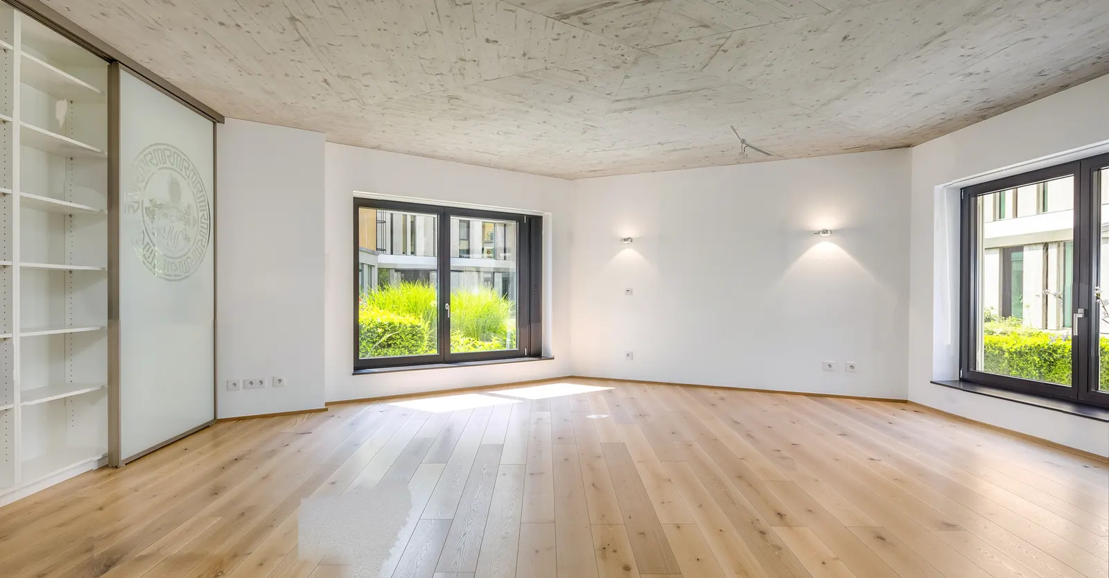 Leeres Wohnzimmer mit Sichtbetondecke und Einbauregal vor dem Home Staging